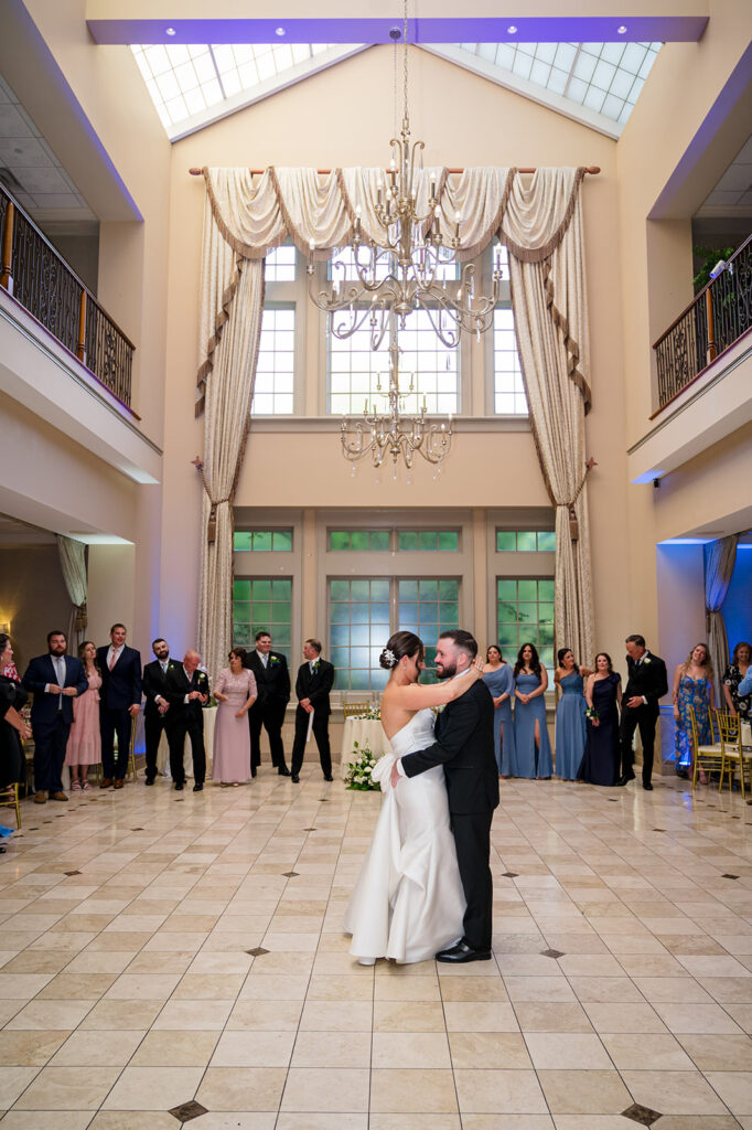 Couple dancing in the Grande Conservatory Ballroom at Talamore Weddings, featuring elegant decor, chandelier, and guests in formal attire celebrating the wedding reception.